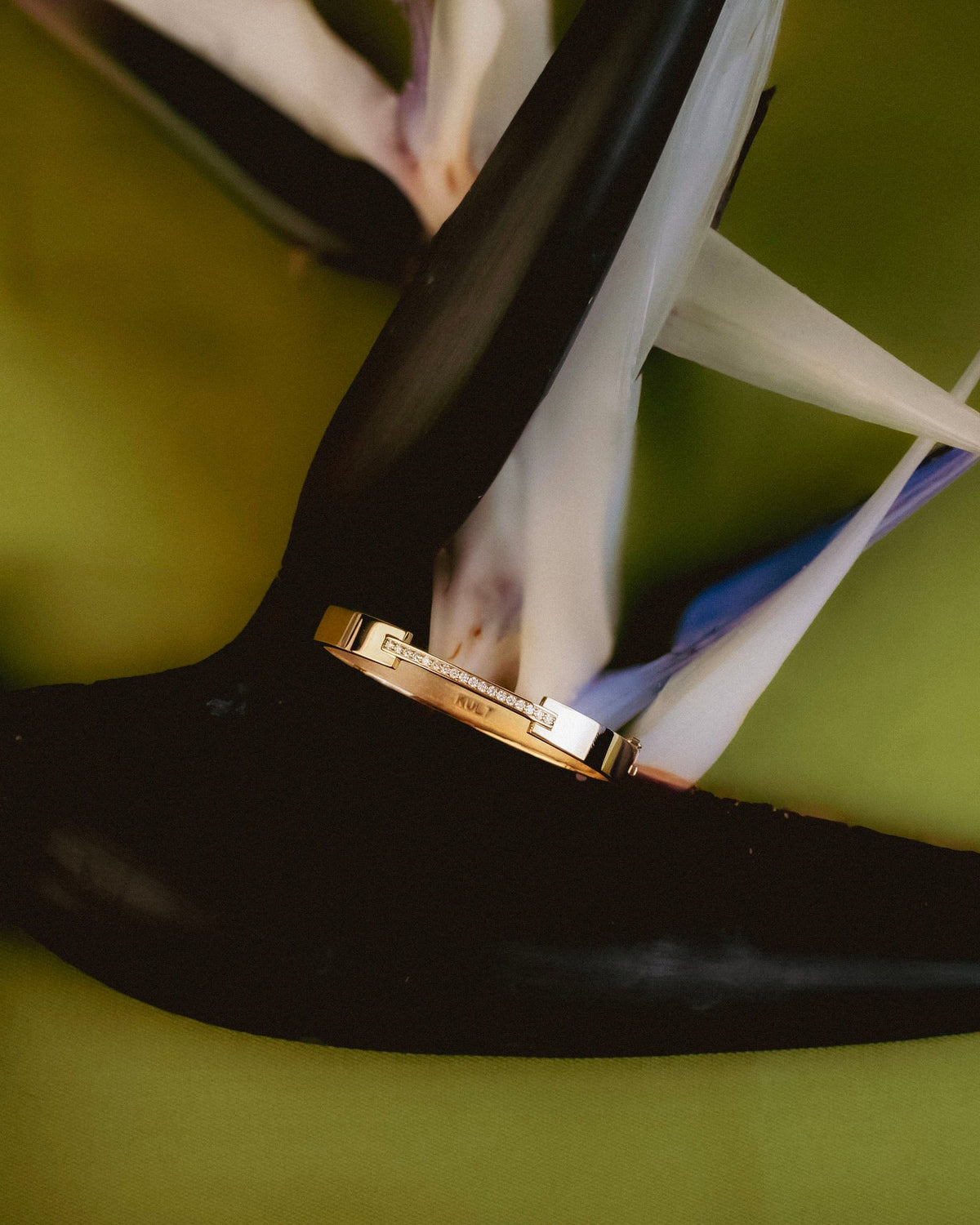 KULT La Ligne gold bangle with a diamond-set bar nestled in the petals of a bird-of-paradise flower (close up)