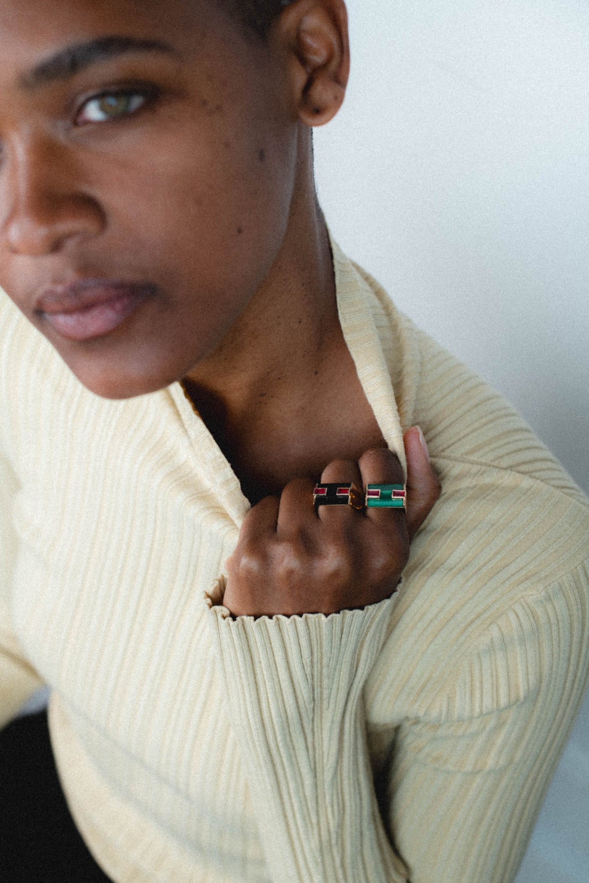 Model in a cream ribbed sweater wearing malachite and onyx rings from the Milestone Collection and touching her collarbone